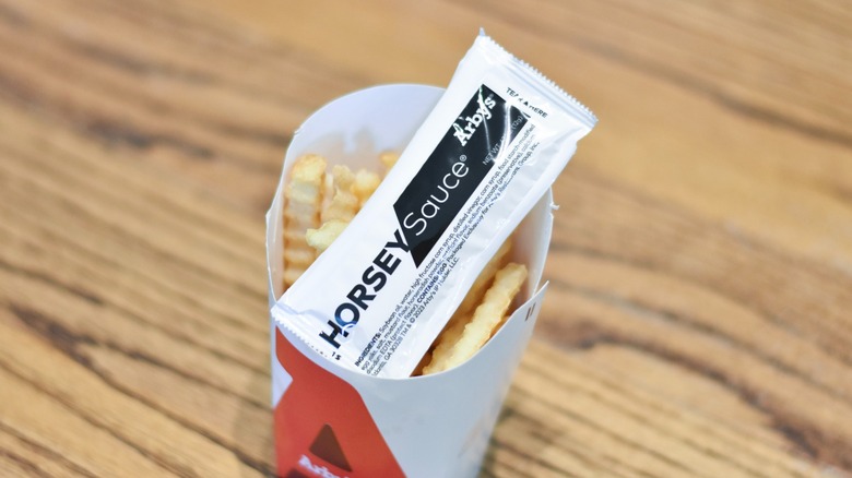 A packet of Arby's horsey sauce on top of a carton of fries