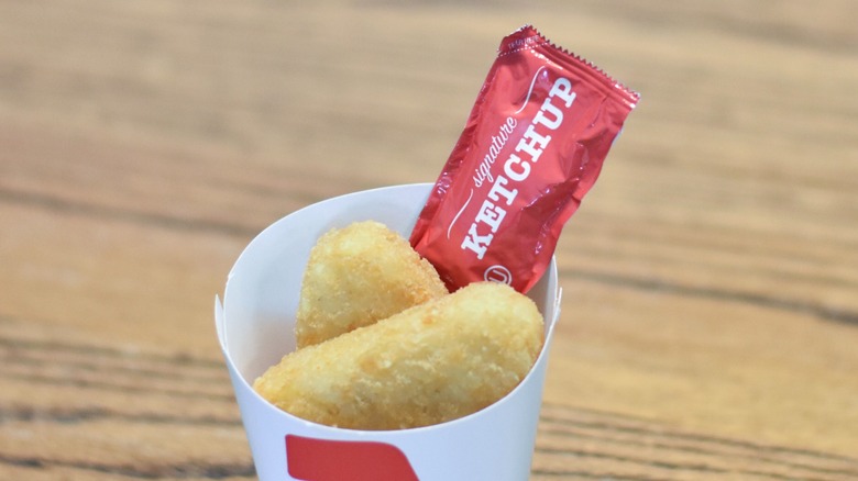 A carton of potato cakes with a ketchup packet on top