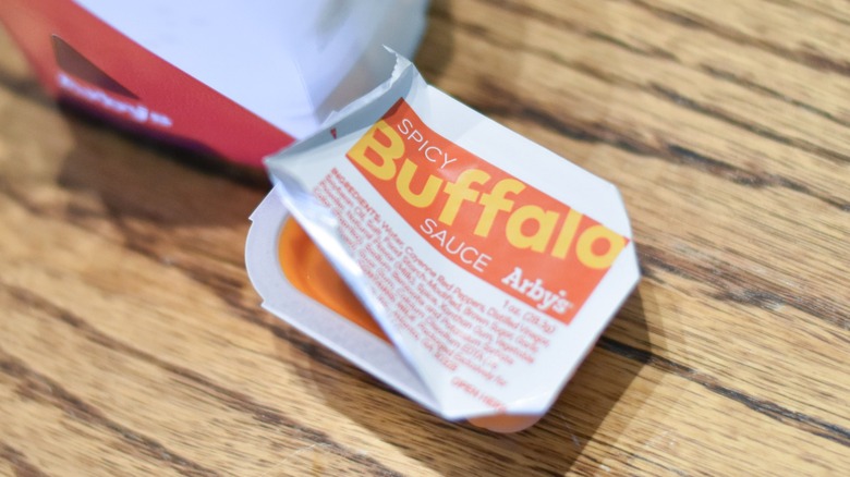A carton of spicy buffalo sauce on a wooden table