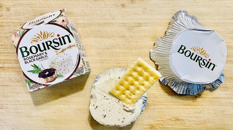 Cracker in opened package of Boursin Rosemary & Black Garlic