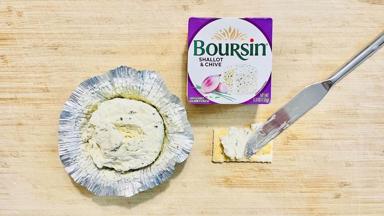 Opened package of Boursin Shallot & Chive with knife and cracker