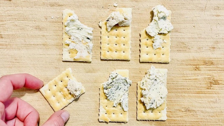 Hand reaching for one of six crackers with various Boursin cheese flavors