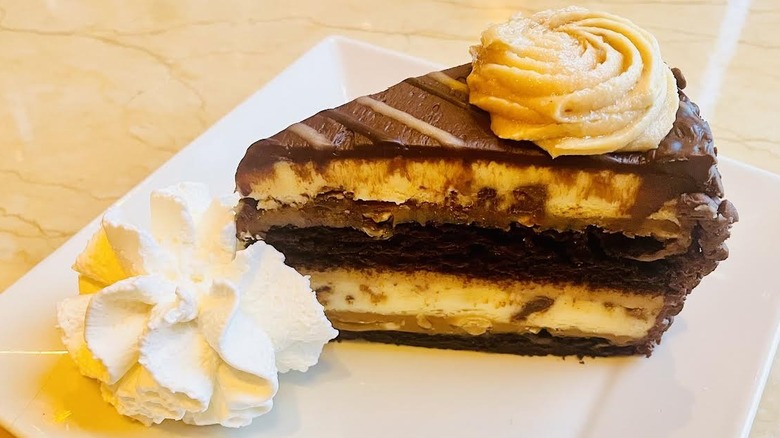 A slice of The Cheesecake Factory's Reese's Peanut Butter Chocolate Cake Cheesecake is shown.