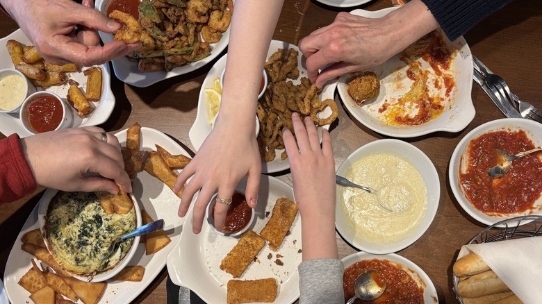hands reaching in to eat Olive Garden food on table