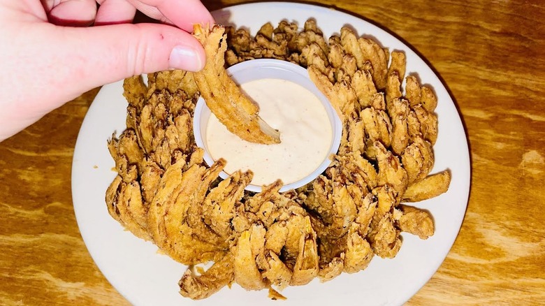 A hand is dipping a piece of Texas Roadhouse Cactus Blossom in sauce.