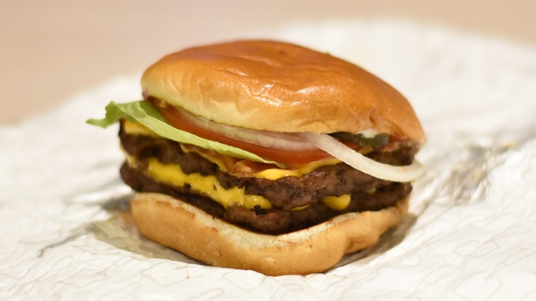 A double stack burger with lettuce, tomato, and onion with cheese on each patty on a bun