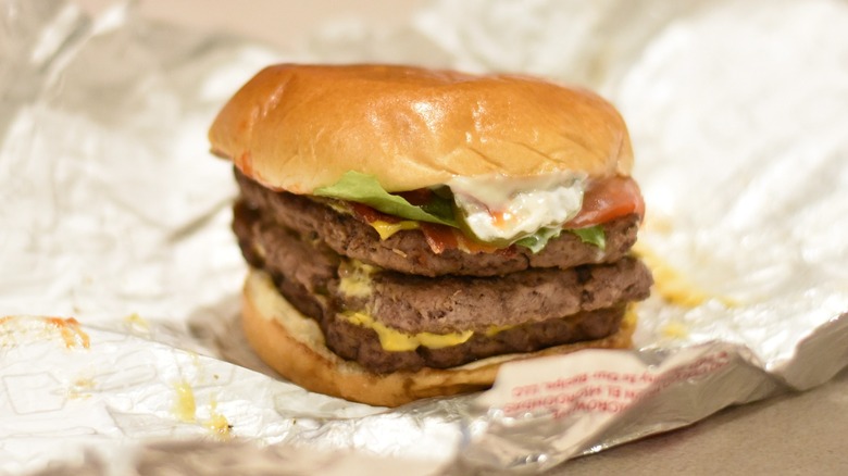 A triple stack burger with lettuce, tomato, and mayo on a bun