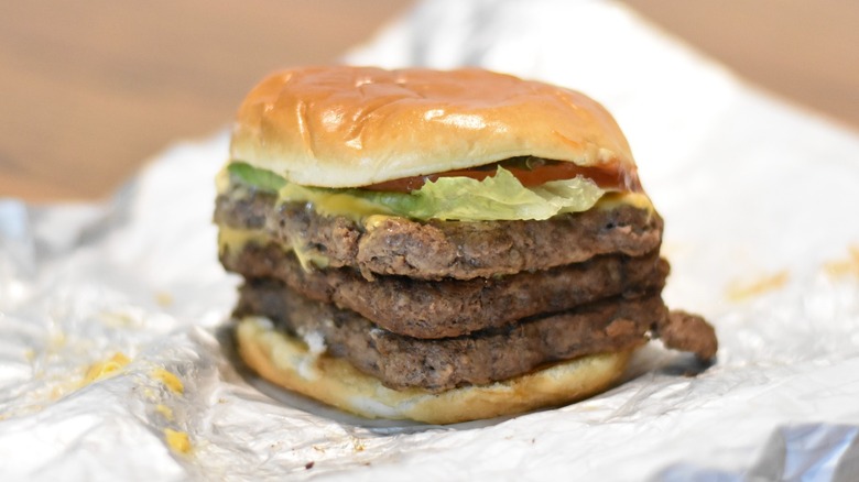 A triple stack burger with lettuce and tomato on a bun