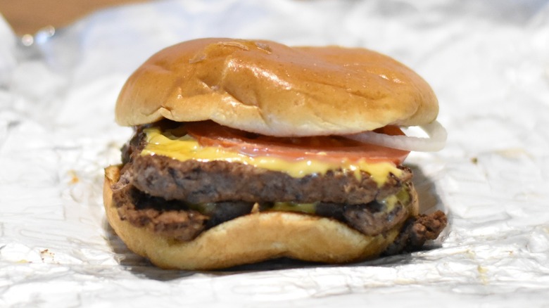 A double burger with cheese, tomato, and onion on a bun