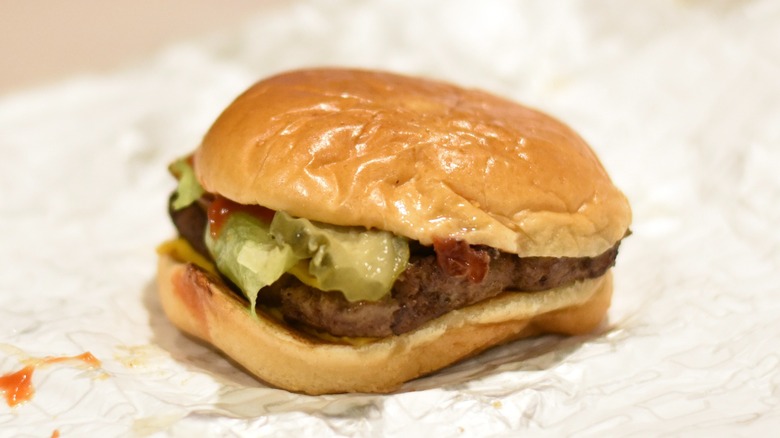 A burger with lettuce, ketchup, and pickles on a bun