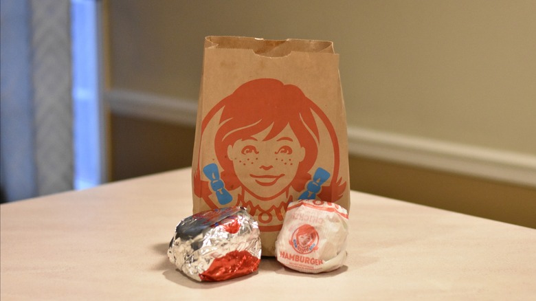 A Wendy's bag with two burgers in wrappers in front