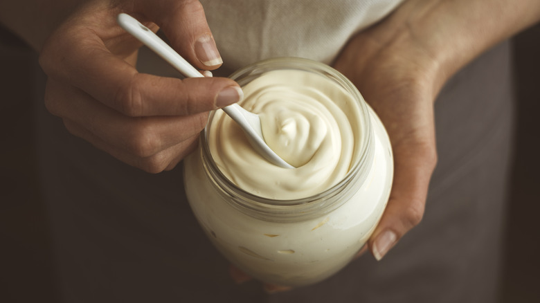 Hand stirring jar of mayonnaise. 