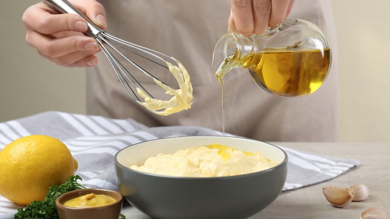 Hand pouring oil into mayonnaise. 