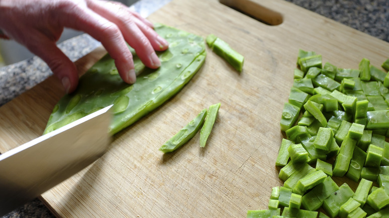 A person cutting a nopal catcus paddle into strips