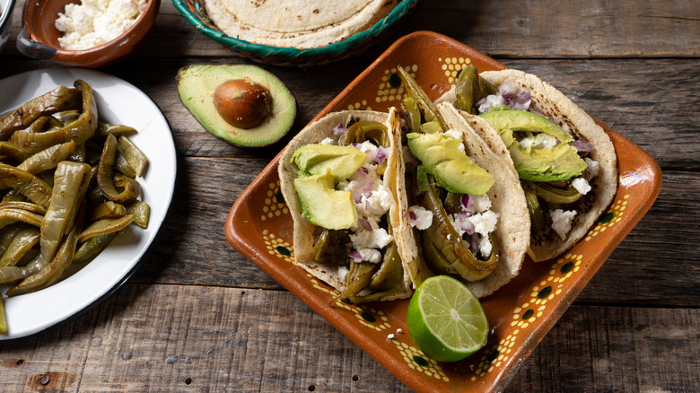 A bowl of cooked nopales next to a plate of nopales tacos