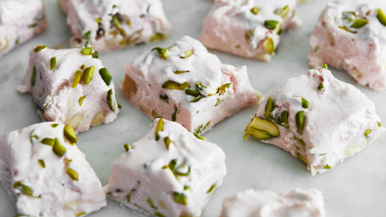 Squares of chewy white nougat filled with pistachios sit on a marble table.