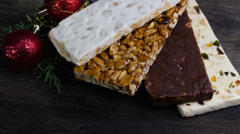 Four varieties of Spanish nougat are placed on a dark wooden table with Christmas decorations.