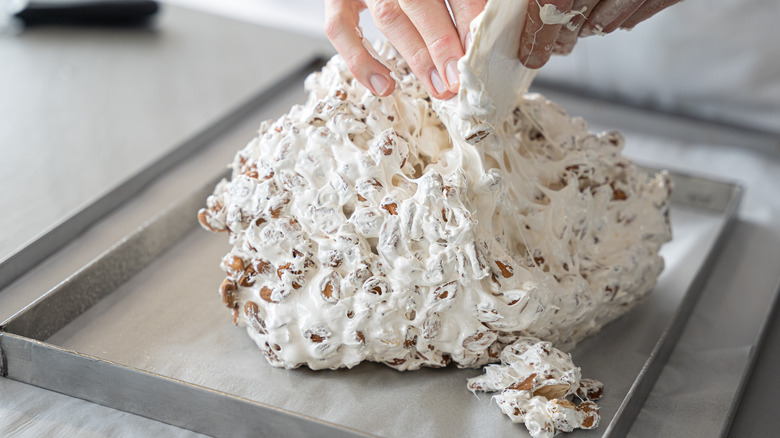 A baker's hands  spreading a nougat mixture into a metal pan.