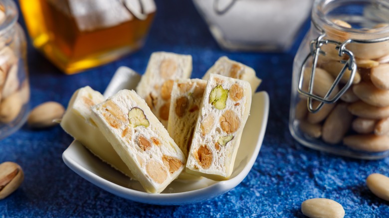 Small nougat pieces and jars of ingredients are arranged on a blue tablecloth.