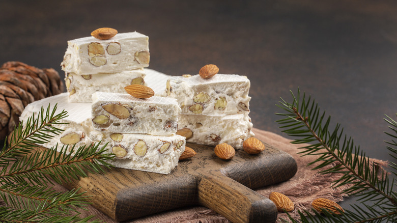 Torrone, soft Italian almond nougat, sits on a wooden cutting board surround by pine branches.