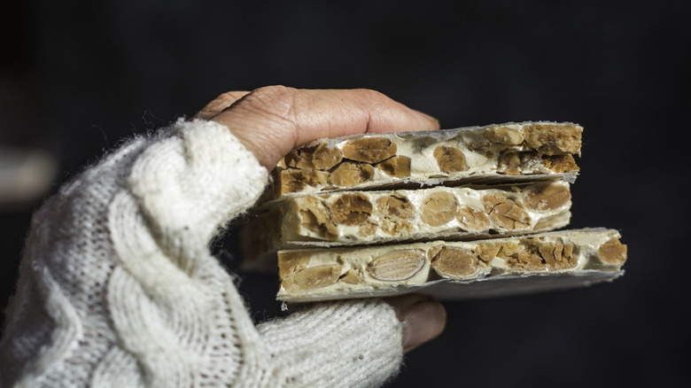 A hand holding hard white nougat filled with nuts.