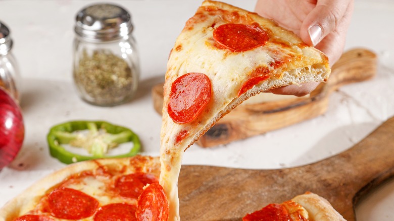 Hand taking pepperoni pizza slice