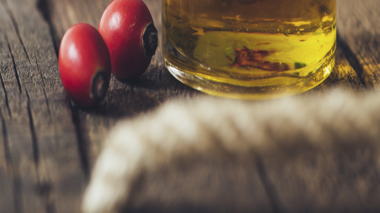 rose hips behind jar of pressed essential oil
