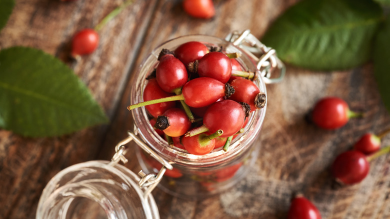 rosehips in clear glass jar on wooden surface
