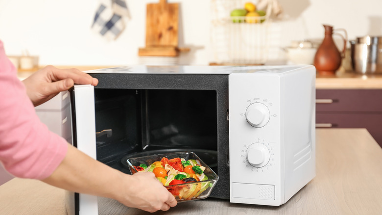 Woman putting vegetables in the microwave