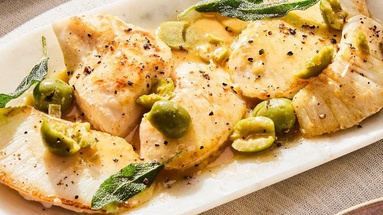 A plate of cooked halibut cheeks seasoned and served with green olives