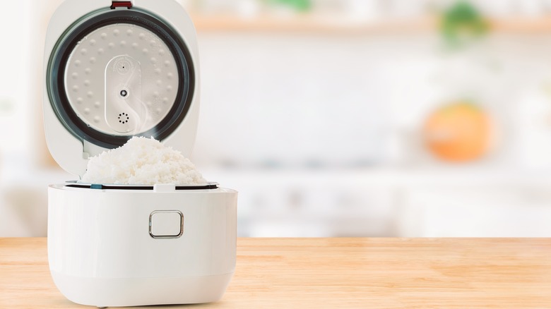 A white rice cooker on a wood  table with blurred kitchen in background