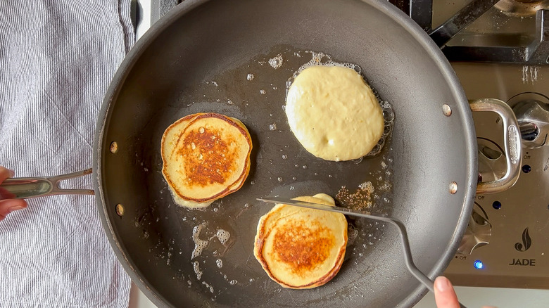 Flipping fluffy lemon ricotta pancakes cooking in pan