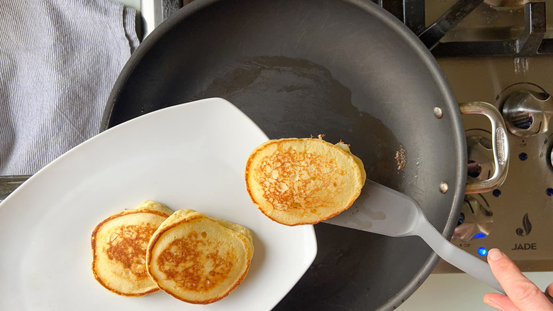 Removing fluffy lemon ricotta pancakes from skillet to platter with spatula