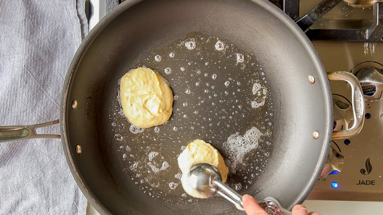 Adding fluffy lemon ricotta pancake batter to skillet with scoop