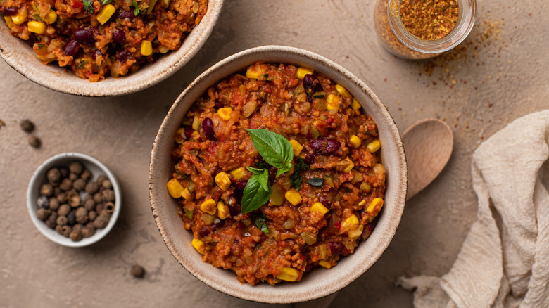 A bowl of vegetable chili with other sides and a wooden spoon
