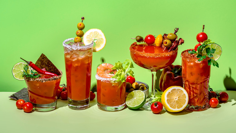 Different glasses of bloody marys against a green background