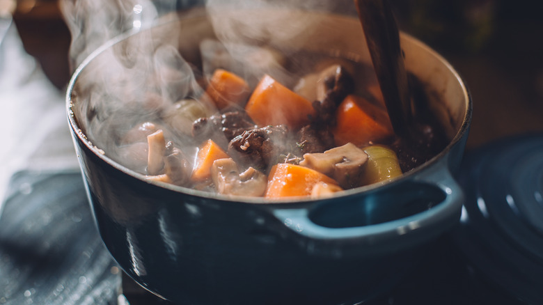 Beef stew in a blue dutch oven with steam coming out