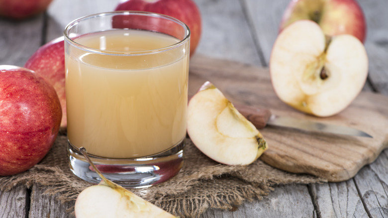 Glass of apple cider surrounded by whole and sliced apples