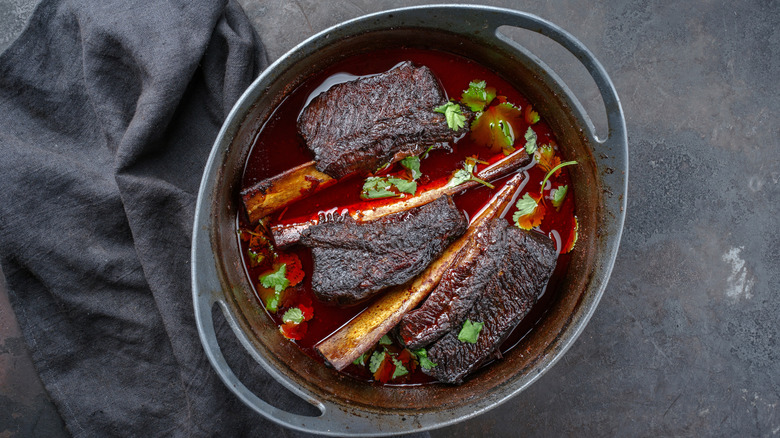 Braised short ribs in pot with fresh herbs