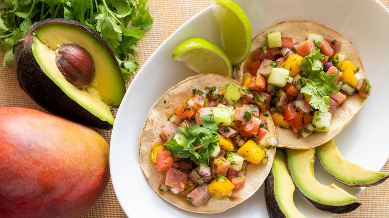Displayed seared tuna tacos in a bowl surrounded by limes and avocados