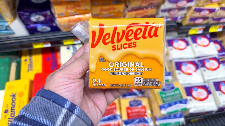 A hand holding a package of Velveeta cheese slices