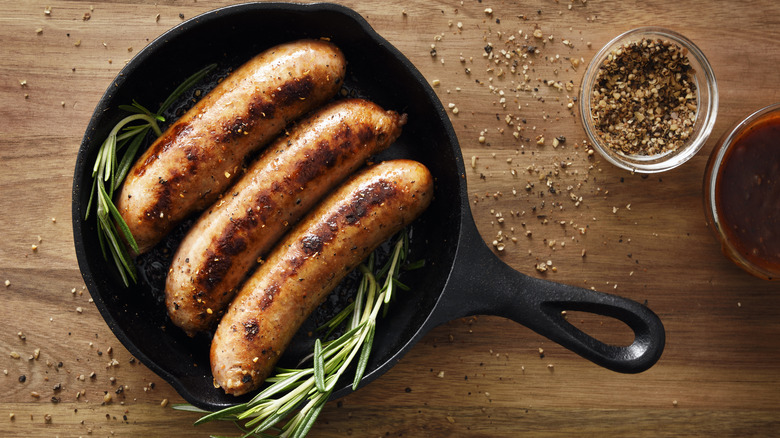 Cooked sausages in a skillet next to sprigs of rosemary