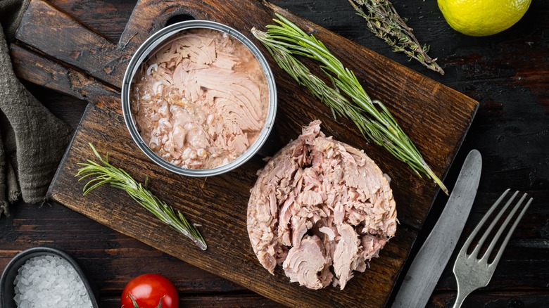 Canned tuna on wooden board with fresh herbs