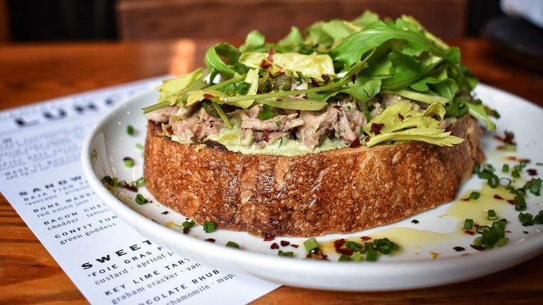 Toast topped with tuna confit, fresh herbs, and greens