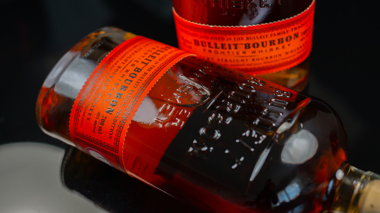 A close-up of two bottles of Bulleit Bourbon, one standing up and one lying on its side.