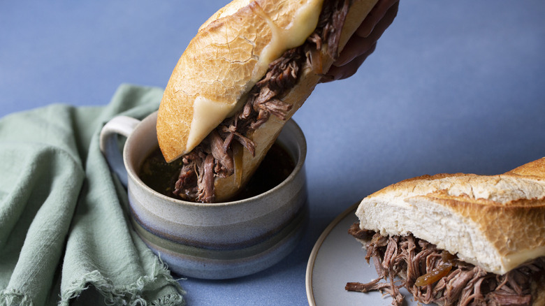 a French dip sandwich being dunked into a cup of au jus