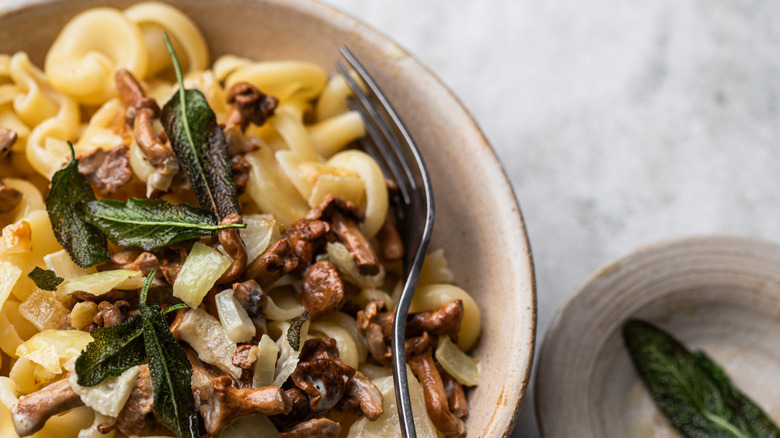 Sage seasoning on a mushroom and onion pasta dish with a fork