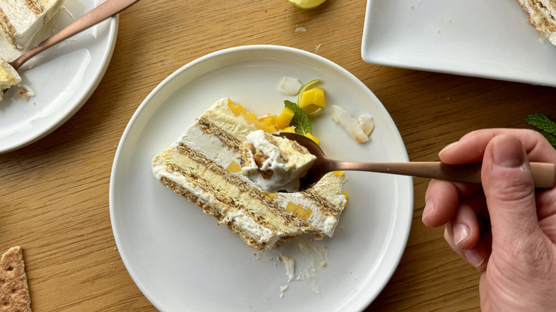 hand holding fork over a slice of whipped cream graham cracker icebox cake with mango