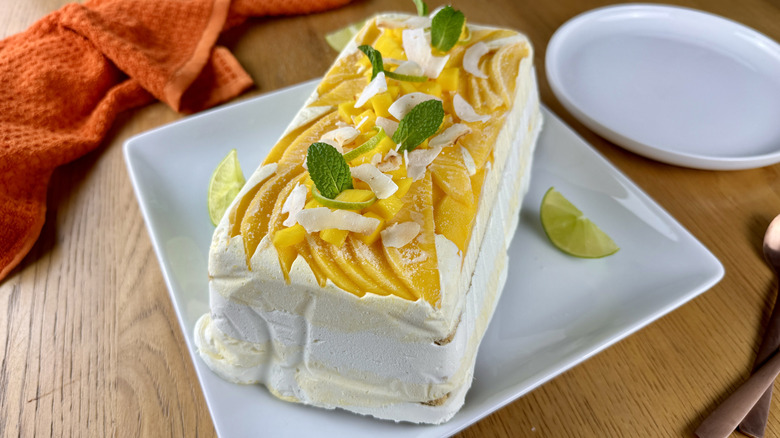 whipped cream graham cracker icebox cake with mango, lime wedges, mint leaves, and coconut