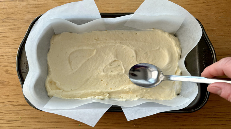 hand holding spoon on top of whipped cream in loaf pan